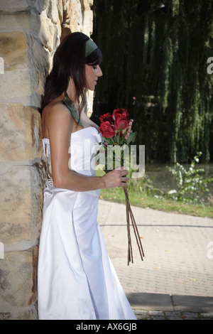 Tedesco-sposa turca si appoggia a stonewall holding rose rosse. Germania, Europa Foto Stock