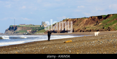 Un uomo che cammina il cane sulla spiaggia Upgang, Sandsend, con Whitby in distanza Foto Stock