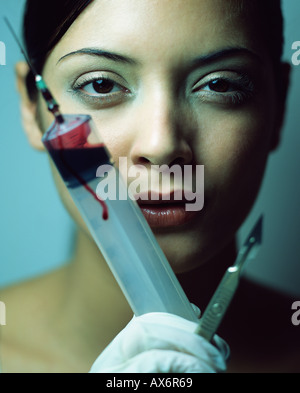 Donna con un bisturi e la siringa di sangue Foto Stock