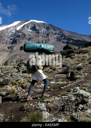 Porter la sacca di custodia sulla sua testa sul Monte Kilimanjaro in Tanzania settentrionale, la montagna più alta in Africa. Foto Stock