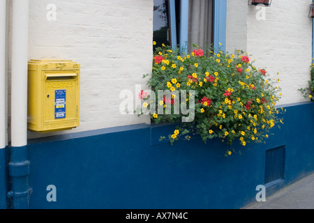 Giallo francese post post sulla parete blu del cottage con i fiori sul davanzale della finestra Foto Stock