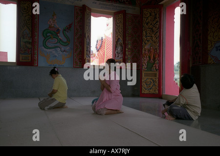 Nuan Naram tempio, Koh Samui, Thailandia. Tre persone che visitano il tempio inginocchiato alla statua del Buddha Foto Stock