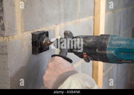 Un edificio la perforazione di 3 pollici (76mm) di fori quadrati in una parete utilizzando un attacco SDS per consentire il montaggio di metallo Scatole da parete per il socket Foto Stock
