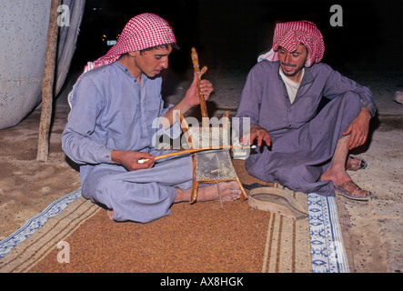 Due uomini beduino in tenda nel deserto siriano. Entrambi siedono su un tappeto. Uno di loro gioca un rababah o rebab, una pelle di capra strumento a corda Foto Stock