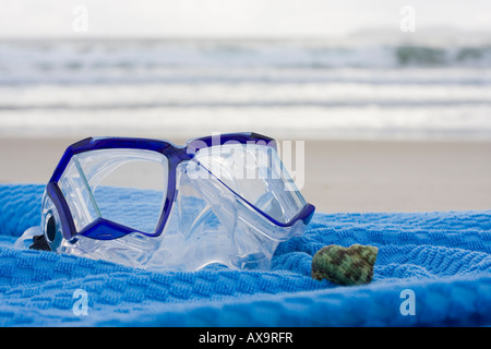 Maschera subacquea e shell su un asciugamano blu sulla spiaggia Foto Stock