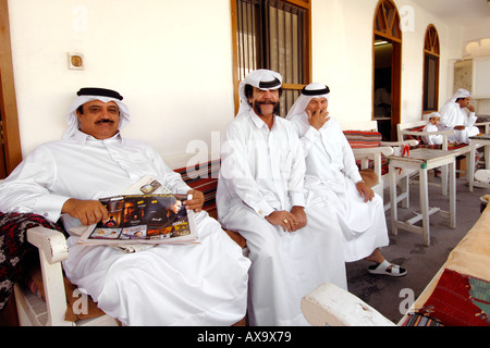 Qataris in abito tradizionale seduta al di fuori di una casa da tè a Doha, capitale del Qatar. Foto Stock