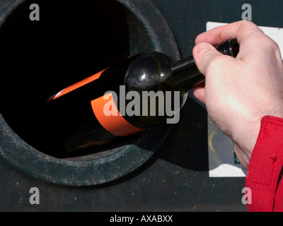 Man mano collocando un vuoto verde bottiglia di vino in un riciclaggio bottle bank bin al deposito di riciclaggio Foto Stock