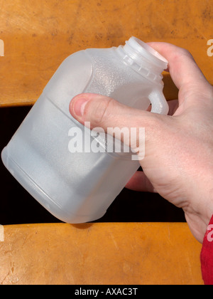 Man mano collocando un vuoto riciclabili pinta opaco latte bottiglia di plastica in un contenitore di riciclaggio al deposito di riciclaggio Foto Stock