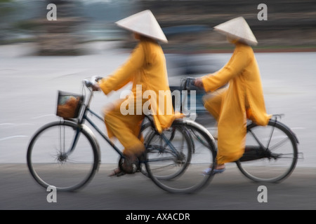 Ragazze in Ao Dai tradizionale vietnamita abito lungo e cappello conico giro in bicicletta sulla strada del Vietnam Foto Stock