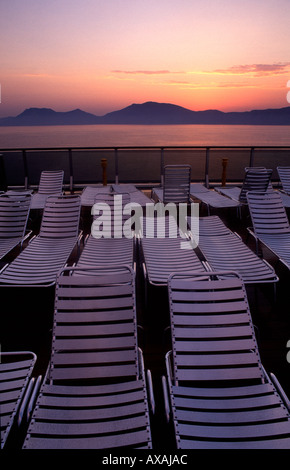 Pila di sedie a sdraio in plastica vuote sul ponte passeggeri della nave da crociera al tramonto. Grecia Foto Stock