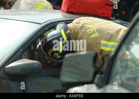 Fire fighter da Ashippun Vigili del Fuoco con la sua testa in vittima s auto prestito finestra di help sulla scena di un incidente di automobile Foto Stock