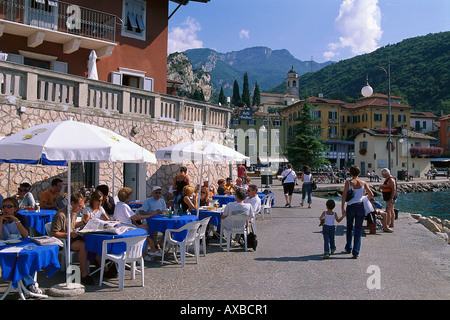 La gente seduta sotto ombrelloni presso un cafè al lungolago, Torbole, Lago di Garda, Trentino, Italia, Europa Foto Stock