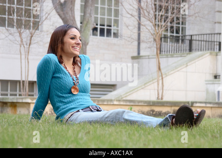 Fotografia di stock di una femmina di studente di college del campus seduto sull'erba Foto Stock