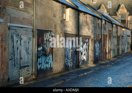 Graffiti sulle porte di garage in un soleggiato piovoso via acciottolata Foto Stock