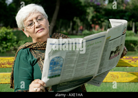 Senior donna leggendo il giornale in un parco Foto Stock