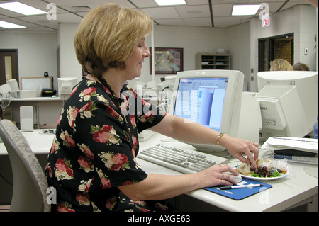 Adulto femmina professionale mangia il pranzo mentre si lavora a un computer al fine di rispettare le scadenze nel suo lavoro Foto Stock