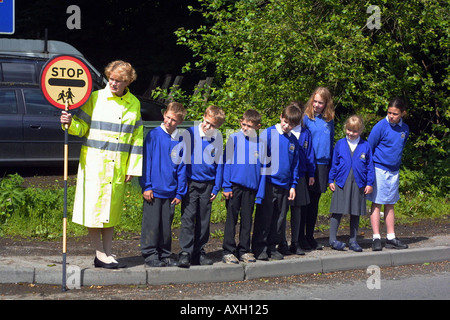 Attraversamento Scuola patrol donna accompagnatori di scolaresche attraverso una strada trafficata dal marciapiede Foto Stock