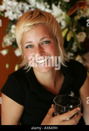 Ritratto di una ridente giovane donna bionda con in mano un bicchiere. Foto Stock
