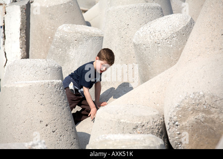 Ragazzo giovane bambino che gioca la scalata su calcestruzzo parete mare difese da Mikrolimano vecchio porto piccolo porto di Pireo o Pireo ad Atene Foto Stock