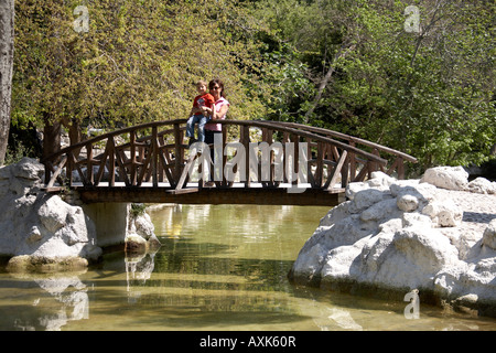 Ragazzo giovane bambino donna e madre sul ponte sullo stagno a primavera tempo in Giardini Nazionali Atene o Athini Grecia Foto Stock