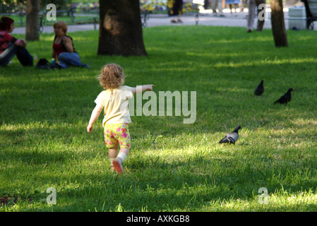 Un bambino a caccia di piccioni in un parco. Foto Stock