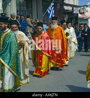 Una linea di Greco sacerdoti ortodossi in abiti colorati di nero da indossare cappelli di cuscinetto e bandiera greca in processione di Pasqua Grecia KOS Foto Stock