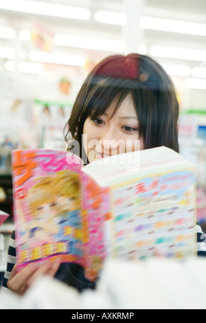 Giovane donna lettura stile manga fumetto, sorridente Foto Stock