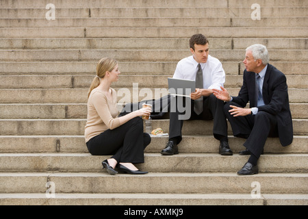 Tre persone business parlando all'aperto sulle scale con il computer portatile Foto Stock