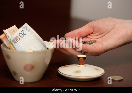 Mano con le monete di fronte ad una tazza di zucchero riempito con le fatture in euro (parte di), close-up Foto Stock
