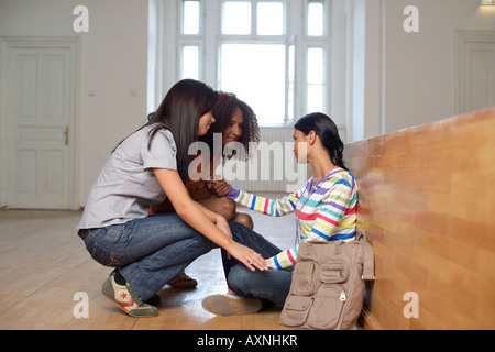 Due giovani donne tifo fino ad un amico che è seduto sul pavimento in un uditivo Foto Stock
