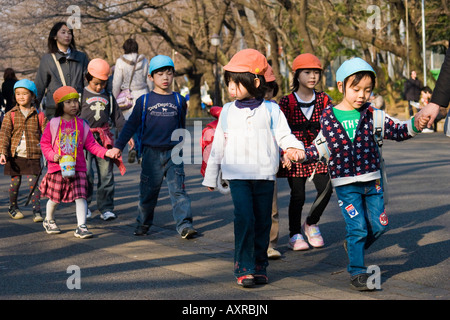 Un giovane giapponese la scuola dei bambini a camminare in una linea tenendo le mani nel Parco di Ueno Tokyo Giappone Foto Stock