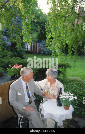 Coppia di anziani che celebra un compleanno o un anniversario insieme con bottiglia di champagne a casa in cortile Foto Stock