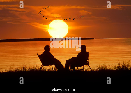 Senior il marito e la moglie sedersi sulla riva del lago Superior vicino Munising Michigan per guardare il tramonto Foto Stock