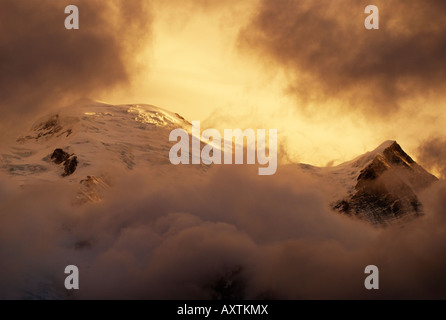 Gli ultimi raggi di sole al tramonto con nubi in chiusura su Snow capped Dôme du Goûter (4304m) e Aig du Goûter (3863m) Foto Stock
