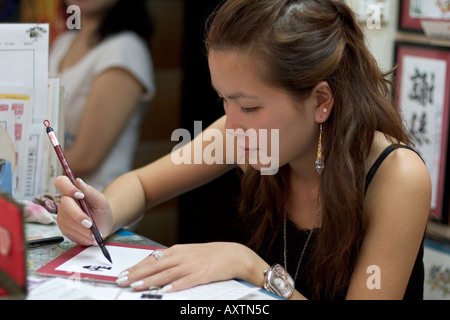 Giovane donna cinese creazione di calligrafia arte su di lei in stallo il Mercato Stanley, Hong Kong Foto Stock