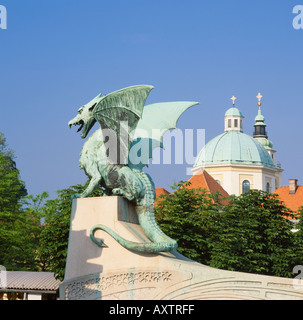 Uno dei quattro draghi sul ponte del drago, Lubiana, Slovenia. Dietro sono le torri della Cattedrale di San Nicola Foto Stock