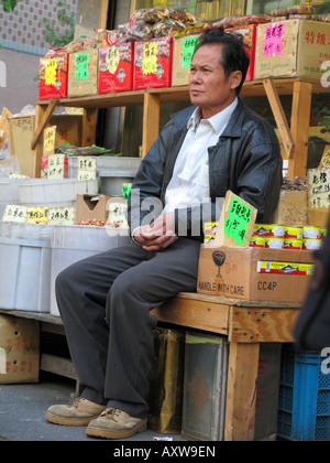 Il venditore si siede tra i suoi prodotti su un mercato in Chinatown, USA, Manhatten, Chinatown, New York Foto Stock