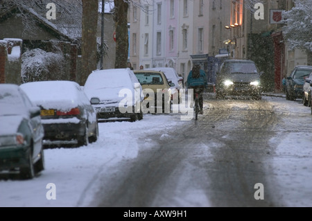 Ciclista senza luci nel traffico di sera dopo la neve invernale Bristol REGNO UNITO. Foto Stock