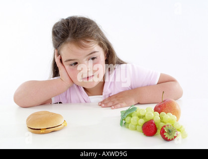 Chubby ragazza con hamburger e frutta fresca, guardando i frutti Foto Stock
