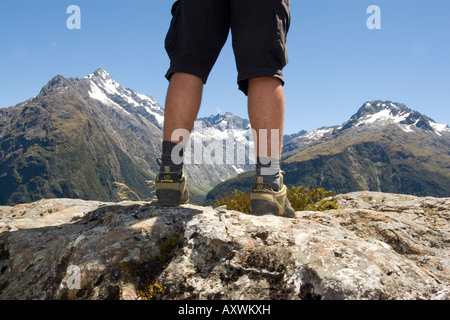 Vista del maschio escursionista gambe su terreno roccioso con le montagne alle spalle Foto Stock