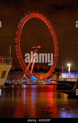 Il 'London Eye" si illumina di rosso durante la notte con barche e del Tamigi in primo piano. Foto Stock
