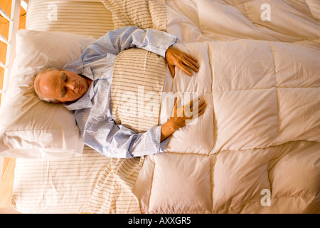 Uomo anziano dormire nel suo pigiama nel suo letto a casa. Egli dorme sul suo retro. Foto Stock