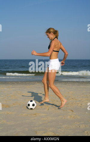 Giovane donna bionda che giocano a calcio in spiaggia Foto Stock