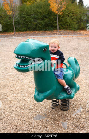 Bimbo di 2 anni a cavallo giocattolo di dinosauri al parco. Foto Stock
