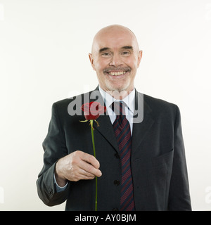 Ritratto in studio isolato su sfondo bianco di un uomo senior tenendo un fiore rosa Foto Stock