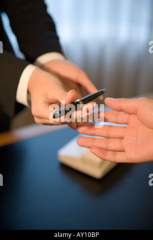Receptionist dando una penna per hotel guest Foto Stock