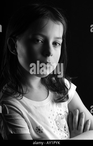 Piuttosto scuro ragazza dai capelli di guardare direttamente la fotocamera con atteggiamento, lato illuminato e sparato contro un sfondo nero Foto Stock