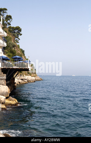 Una terrazza che si affaccia sulla baia di Napoli (Napoli) con ombrelloni blu costruita su un affioramento di rocce Foto Stock