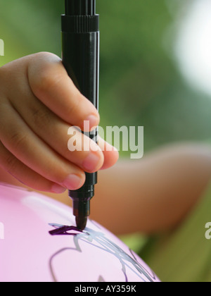 Close-up di un bambino del disegno a mano su un palloncino con un pennarello Foto Stock