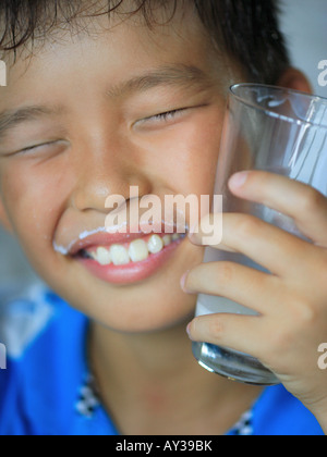 Close-up di un ragazzo con in mano un bicchiere e sorridente con il latte di baffi Foto Stock